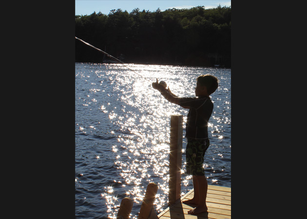 Capturing the fun of a boy fishing off a dock on Lake Sunapee as the setting sun shimmers on the lake by Echo Cove Photography