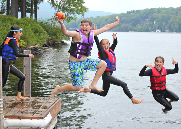 Capturing the fun of kids making crazy jumps together off a dock at Lake Sunapee in the summer by Echo Cove Photography